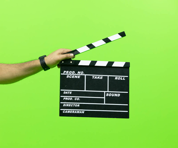 Men's hand holding camera slate for the filming isolated on green background. clapperboard in chroma - Photo, Image