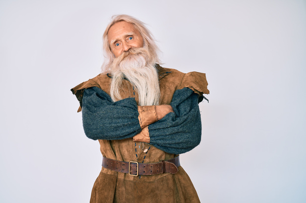 Vieil homme âgé aux cheveux gris et à la barbe longue portant un costume traditionnel viking heureux visage souriant avec les bras croisés regardant la caméra. personne positive.  - Photo, image