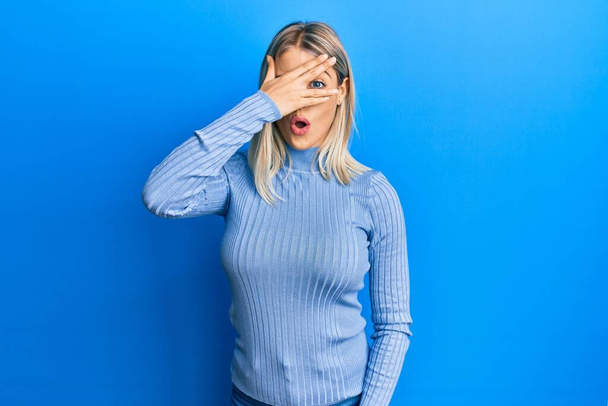 Beautiful blonde woman wearing casual clothes peeking in shock covering face and eyes with hand, looking through fingers with embarrassed expression.  - Photo, Image