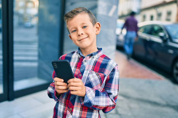 Imádnivaló kaukázusi fiú mosolyog boldog segítségével okostelefon a városban. - Fotó, kép