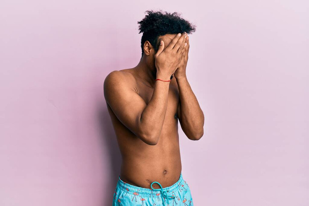 Молодий афроамериканець з бородою в купальнику з сумним виразом, закриваючи обличчя руками під час плачу. Концепція депресії.  - Фото, зображення