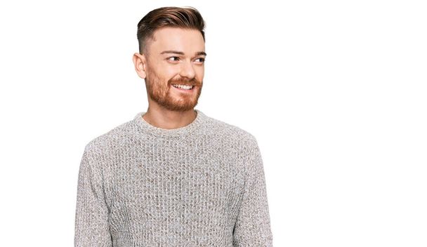 Young redhead man wearing casual winter sweater looking away to side with smile on face, natural expression. laughing confident.  - Фото, изображение