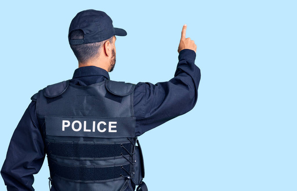 Mladý hispánec v policejní uniformě pózující pozpátku ukazuje prstem dopředu  - Fotografie, Obrázek