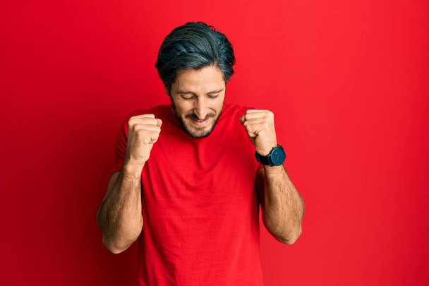 Young hispanic man wearing casual red t shirt excited for success with arms raised and eyes closed celebrating victory smiling. winner concept.  - Foto, Imagen