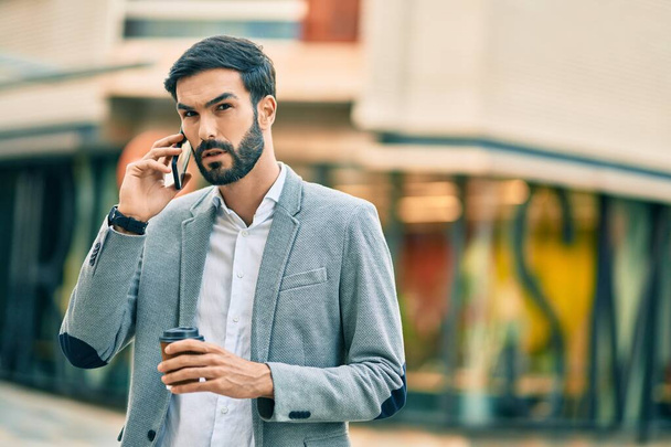 Ciddi bir ifadeyle genç İspanyol işadamı akıllı telefondan konuşuyor ve şehirde kahve içiyor.. - Fotoğraf, Görsel