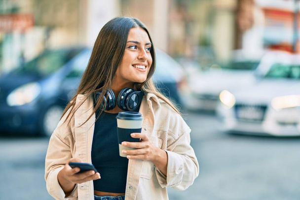 Jeune fille hispanique utilisant smartphone et boire emporter du café au parc. à la ville. - Photo, image