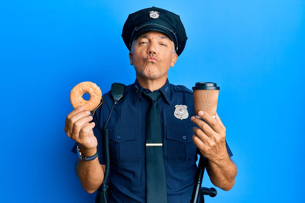 Handsome middle age mature police man eating donut and drinking coffee looking at the camera blowing a kiss being lovely and sexy. love expression.  - Fotó, kép