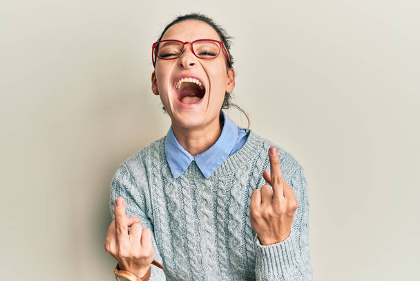 Young caucasian woman wearing casual clothes and glasses showing middle finger doing fuck you bad expression, provocation and rude attitude. screaming excited  - Foto, immagini