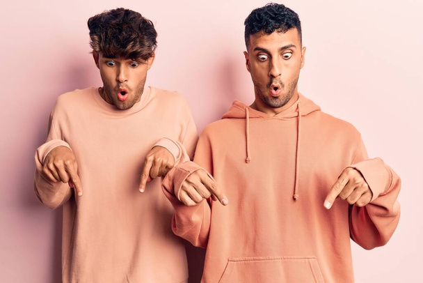 junges schwules Paar in lässiger Kleidung zeigt mit Fingern auf Werbung, überraschtem Gesicht und offenem Mund nach unten  - Foto, Bild