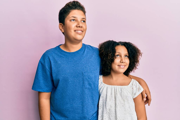 Young hispanic family of brother and sister wearing casual clothes together looking away to side with smile on face, natural expression. laughing confident.  - Zdjęcie, obraz