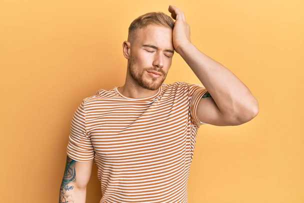 Young caucasian man wearing casual striped t-shirt surprised with hand on head for mistake, remember error. forgot, bad memory concept.  - Fotoğraf, Görsel