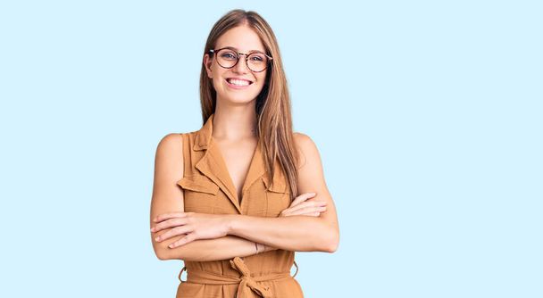 Young beautiful blonde woman wearing casual clothes and glasses happy face smiling with crossed arms looking at the camera. positive person.  - Foto, Imagen