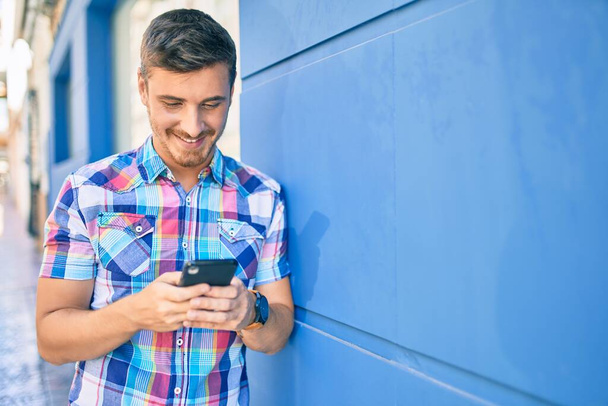 Fiatal kaukázusi férfi mosolyog boldog segítségével okostelefon a városban. - Fotó, kép