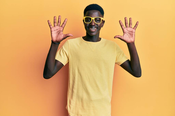 Genç Afro-Amerikalı günlük kıyafetler ve gözlük takmış on numaralı parmaklarıyla onu gösterirken kendinden emin ve mutlu gülümsüyor..  - Fotoğraf, Görsel