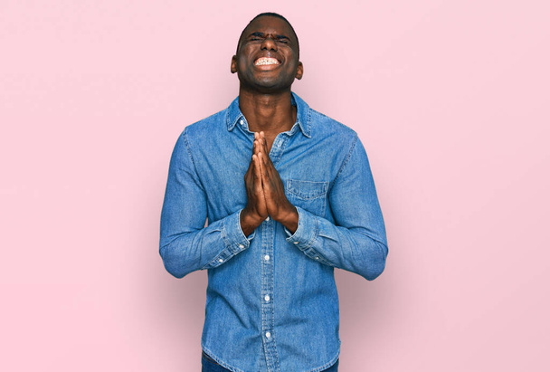 Jonge Afro-Amerikaanse man draagt casual kleding bedelen en bidden met de handen samen met hoop uitdrukking op het gezicht zeer emotioneel en bezorgd. bedelen.  - Foto, afbeelding