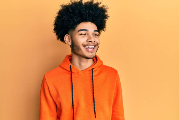 Afro saçlı, sıradan bir kazak giyen, rahat bir görünüm takınan, kendine güvenen ve gülümseyen Afro-Amerikan genç adam..  - Fotoğraf, Görsel