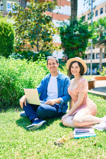 Hermosa pareja sonriendo feliz sentado en la hierba usando el ordenador portátil en el parque - Foto, imagen