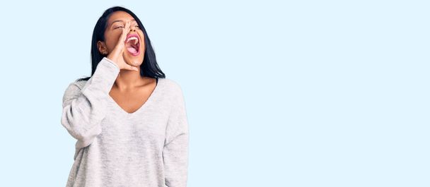 Hispanic woman with long hair wearing casual clothes shouting and screaming loud to side with hand on mouth. communication concept.  - Photo, Image