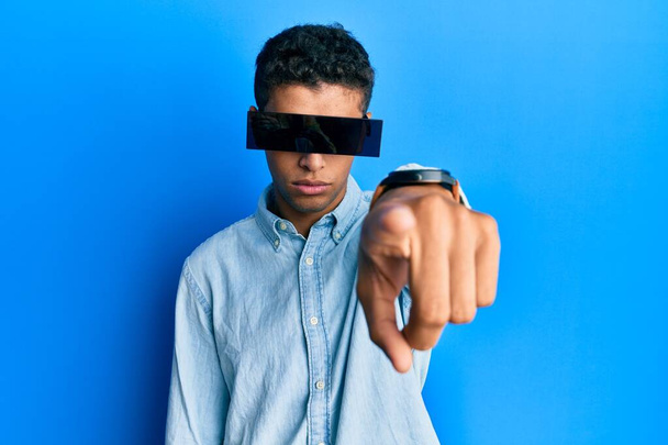 Mladý pohledný africký Američan s bannerovými brýlemi zakrývajícími oči ukazující prstem na fotoaparát a na vás, sebevědomé gesto vypadá vážně  - Fotografie, Obrázek