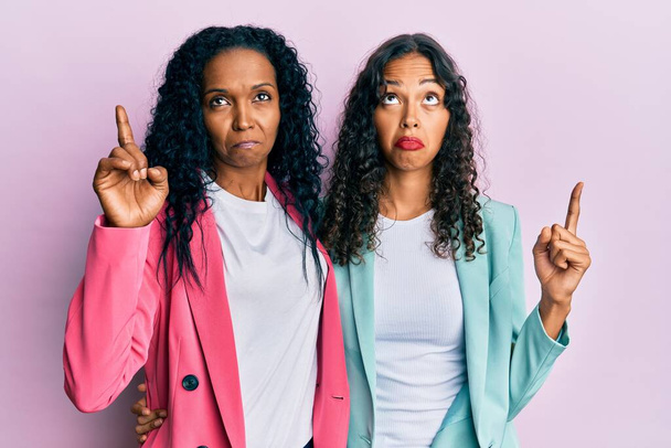 Az afro-amerikai anya és lánya üzleti stílust visel, szomorúnak és feldúltnak tűnik, jelezve az irányt az ujjaival, boldogtalan és depressziós..  - Fotó, kép