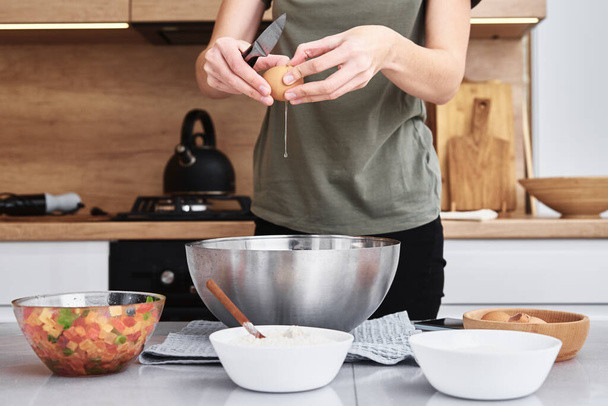 Женщина на кухне готовит тесто. Руки разбивают яйцо в миску - Фото, изображение