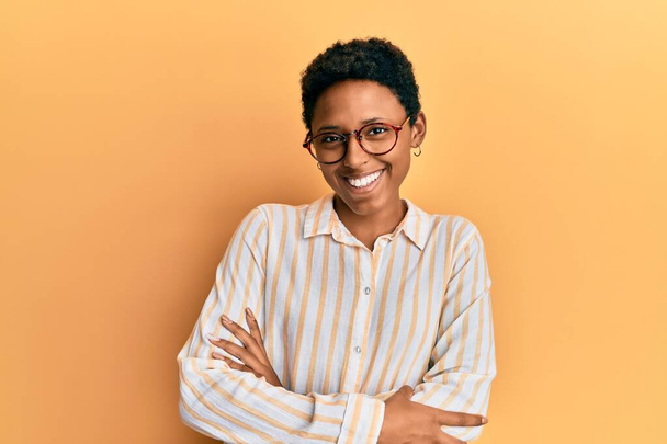 Young african american girl wearing casual clothes and glasses happy face smiling with crossed arms looking at the camera. positive person.  - Zdjęcie, obraz