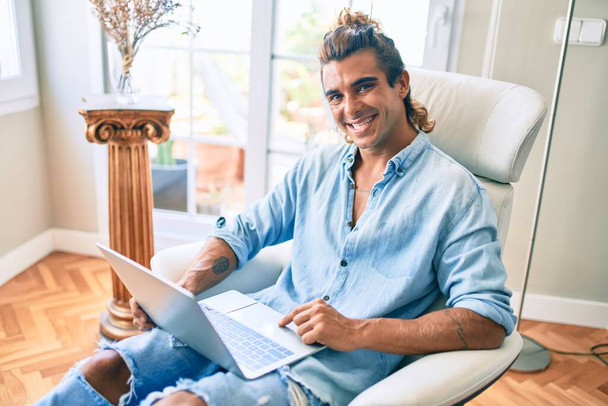 Young hispanic man smiling happy using laptop at home - 写真・画像
