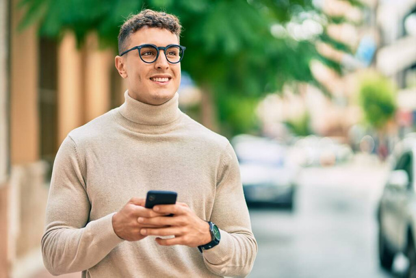 Młody Latynos w okularach za pomocą smartfona w mieście. - Zdjęcie, obraz