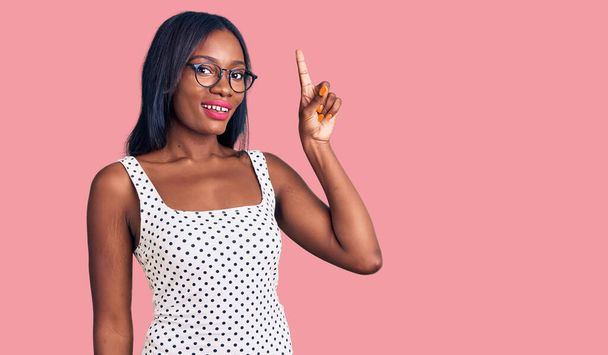 Young african american woman wearing casual clothes and glasses pointing finger up with successful idea. exited and happy. number one.  - Foto, Imagem