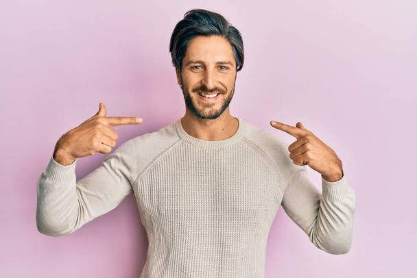 Молодий іспаномовний чоловік в повсякденному зимовому светрі усміхається весело показуючи і вказуючи пальцями зуби і рот. концепція здоров'я зубів
.  - Фото, зображення