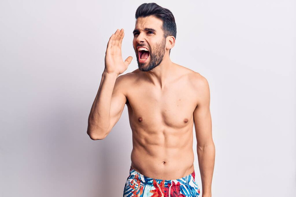 Young handsome man with beard shirtless wearing swimwear shouting and screaming loud to side with hand on mouth. communication concept.  - Fotó, kép