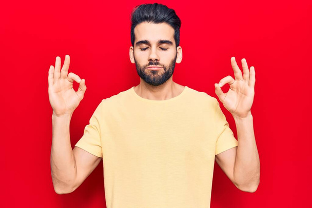Young handsome man with beard wearing casual t-shirt relax and smiling with eyes closed doing meditation gesture with fingers. yoga concept.  - Fotoğraf, Görsel