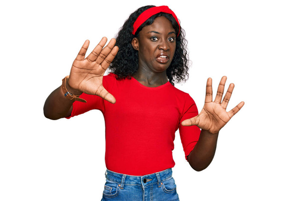 Красивая африканская молодая женщина в повседневной одежде, испуганная и испуганная выражением страха, прекращает жесты руками, крича в шоке. концепция паники.  - Фото, изображение