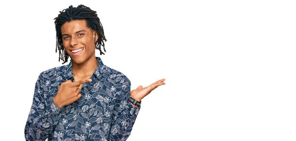 Jonge Afro-Amerikaanse man draagt jaren '80 shirt verbaasd en glimlachend naar de camera terwijl presenteren met de hand en wijzen met de vinger.  - Foto, afbeelding