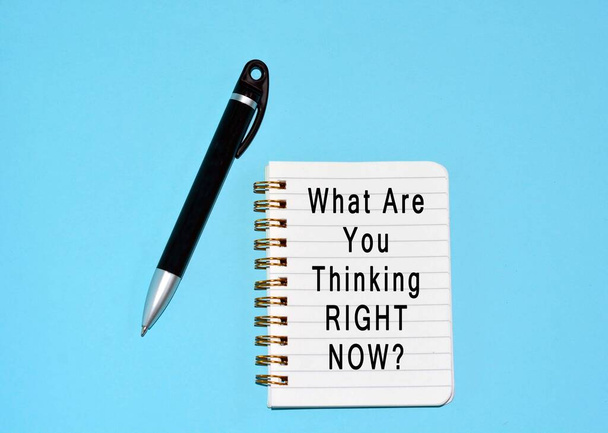 Text written on note pad and a pen with blue background. What are you thinking right now - Photo, Image