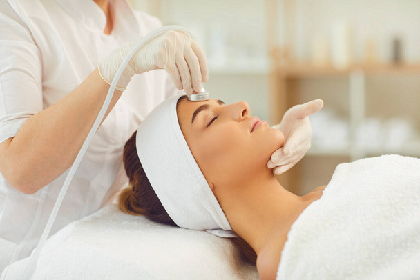 Woman getting facial skin ultrasound cavitation and anti-aging cosmetics from cosmetologist - Photo, Image