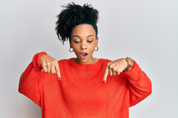 Jeune fille afro-américaine portant des vêtements décontractés pointant vers le bas avec les doigts montrant la publicité, visage surpris et bouche ouverte  - Photo, image