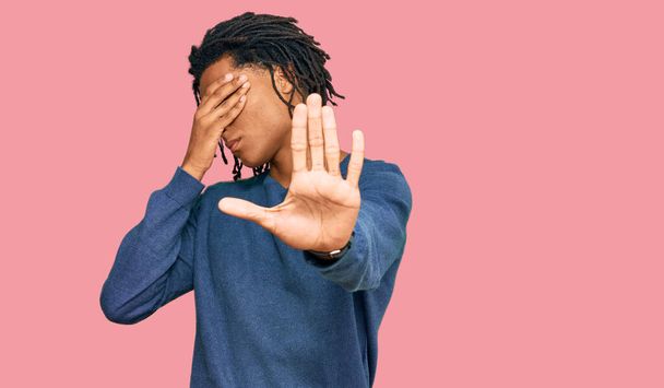 Jonge Afro-Amerikaanse man draagt casual winter trui die ogen bedekt met handen en doet stop gebaar met droevige en angst uitdrukking. beschaamd en negatief concept.  - Foto, afbeelding