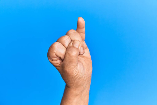 Рука старшего латиноамериканца на синем изолированном фоне показывает мизинец в качестве обещания на мизинце, номер один  - Фото, изображение