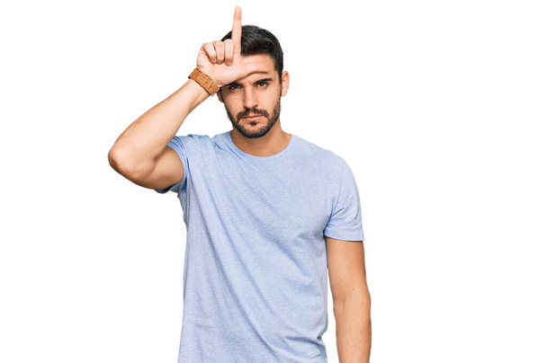 Jonge Latijns-Amerikaanse man draagt casual kleding lachen van mensen met vingers op het voorhoofd doen verliezer gebaar bespotten en beledigen.  - Foto, afbeelding