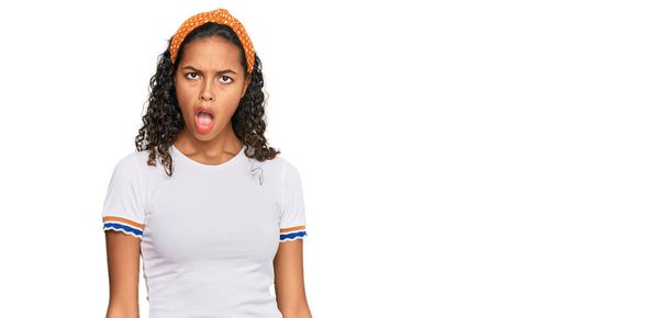 Jeune fille afro-américaine portant des vêtements décontractés dans le visage de choc, l'air sceptique et sarcastique, surpris avec la bouche ouverte  - Photo, image