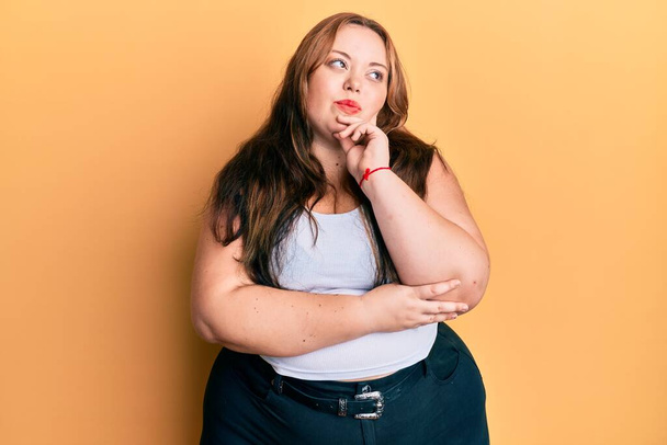 Plus size caucasian young woman wearing casual clothes thinking concentrated about doubt with finger on chin and looking up wondering  - Фото, изображение