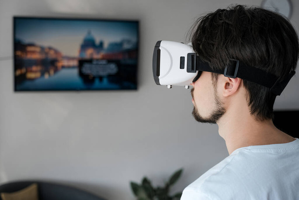 Молодой человек энергично играет в видеоигру виртуальной реальности в VR очках. Мужчина играет в видеоигры. Время отдыхает. Радостные выходные. Многопользовательская игра. Онлайн игры. Потоковые игры. - Фото, изображение