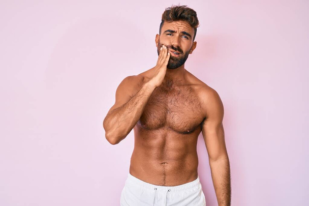 Young hispanic man standing shirtless touching mouth with hand with painful expression because of toothache or dental illness on teeth. dentist  - Photo, Image