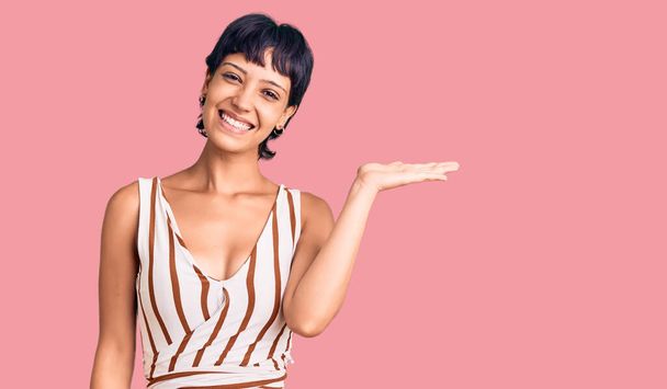 Young brunette woman with short hair wearing summer outfit smiling cheerful presenting and pointing with palm of hand looking at the camera.  - Photo, Image