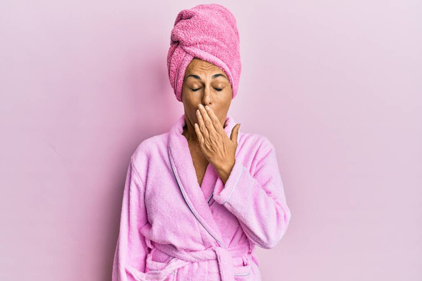 Middle age hispanic woman wearing shower towel cap and bathrobe bored yawning tired covering mouth with hand. restless and sleepiness.  - Fotoğraf, Görsel