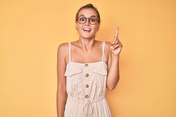 Mooie blanke vrouw draagt zomerjurk wijzende vinger omhoog met een succesvol idee. opgewonden en gelukkig. Nummer een.  - Foto, afbeelding