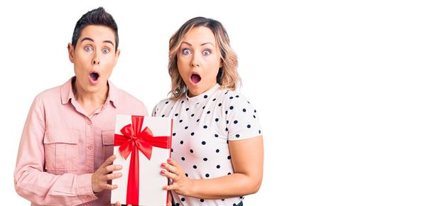 Couple of women holding gift scared and amazed with open mouth for surprise, disbelief face  - Photo, Image