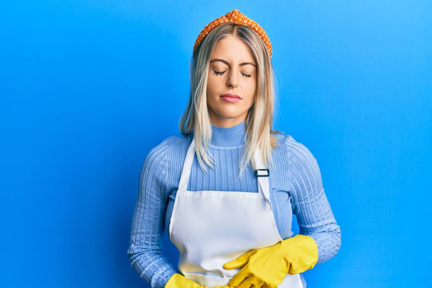Beautiful blonde woman wearing cleaner apron and gloves with hand on stomach because indigestion, painful illness feeling unwell. ache concept.  - Photo, image