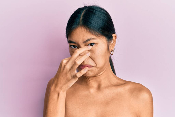 若い中国の女性は、鼻の上に指で息を保持し、皮膚のにおいが何か臭くて嫌な、耐え難い匂いを示すトップレス立っている。臭いが悪い  - 写真・画像